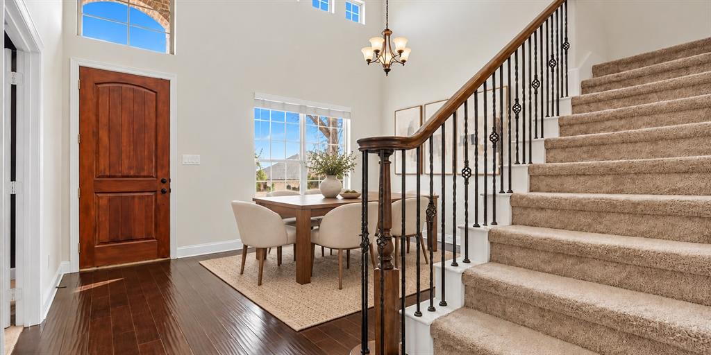 Double-height entryway featuring dark wood-finish flooring, a multi-pane arched transom window, a wood-finish entry door, and a staircase with an ornamental metal balustrade and wood handrail