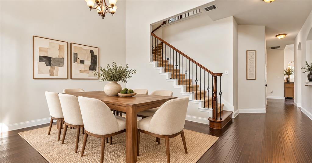 High-ceiling interior space featuring wood-finish flooring, a staircase with a wooden handrail and iron balusters, and a tiered chandelier