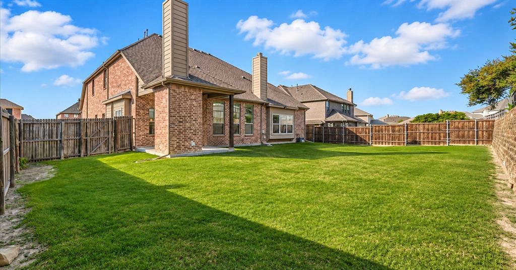 Backyard featuring a brick exterior, two masonry chimneys, a covered patio, and perimeter wood fencing surrounding a grass lawn