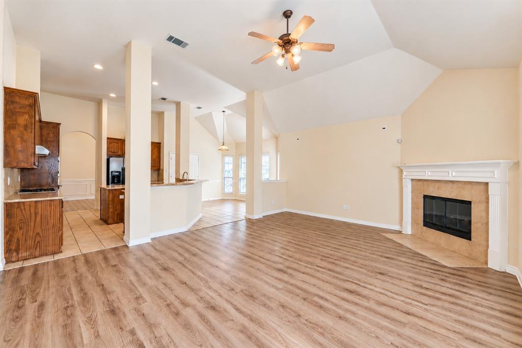 Vaulted ceilings, wood-look LVP flooring, fireplace with a mantle, recessed lighting, and kitchen cabinetry