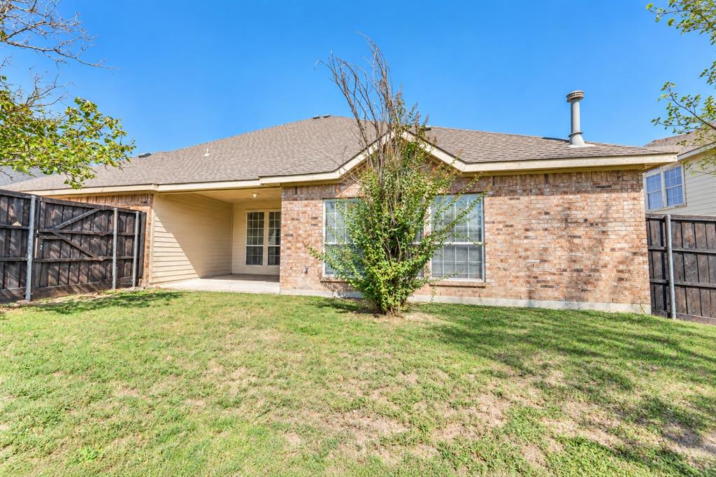 Rear exterior featuring a brick facade, covered concrete patio, asphalt shingle roof, and wooden privacy fencing