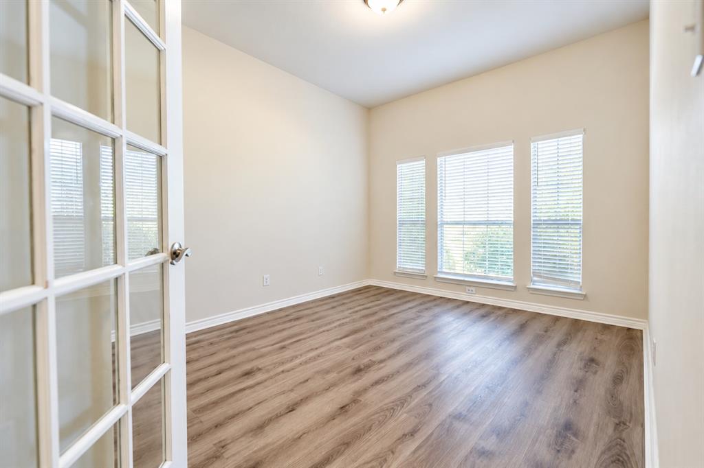 Room featuring wood-look LVP flooring, neutral wall paint, three large windows with horizontal blinds, and a glass-paneled French door
