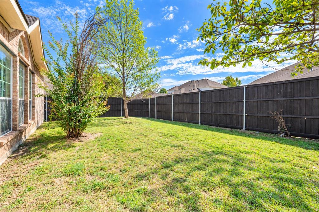 Rear exterior featuring a brick facade, manicured lawn, and full-height wood fencing