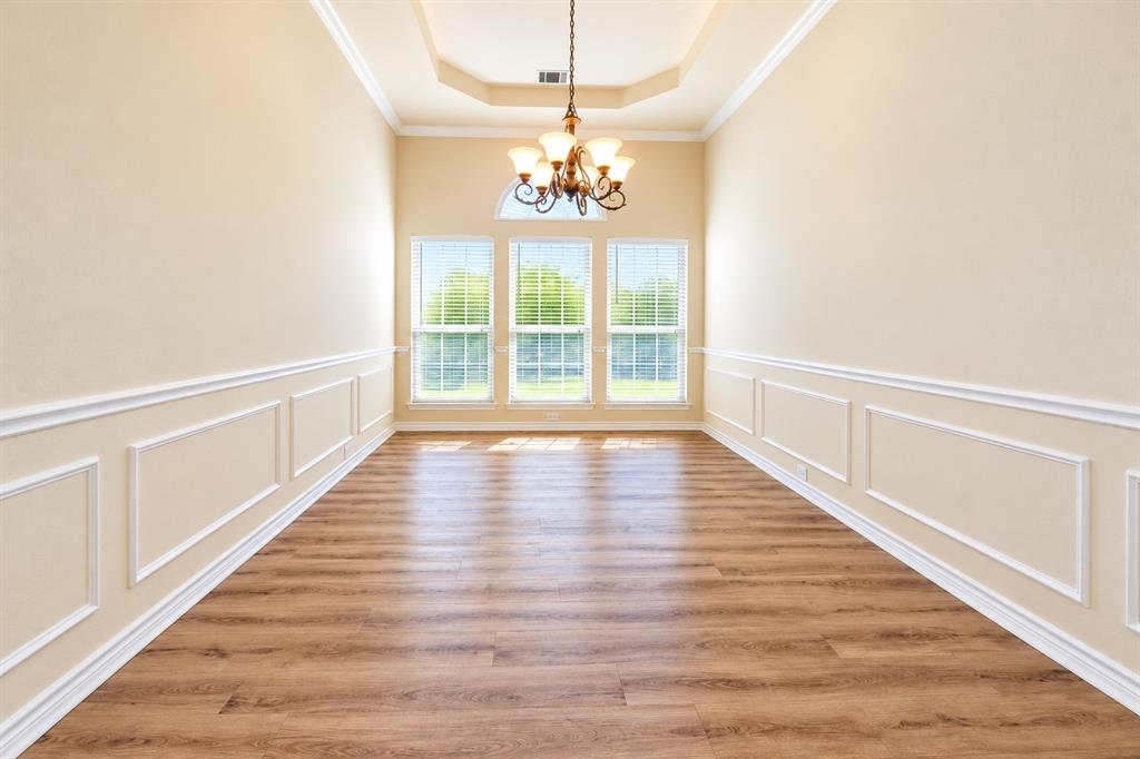 Formal dining room featuring wood-look LVP flooring, wainscoting, a tray ceiling, an arched window, and a multi-arm chandelier Formal dining room featuring wood-look LVP flooring, wainscoting, a tray ceiling, an arched window, and a multi-arm chandelier
