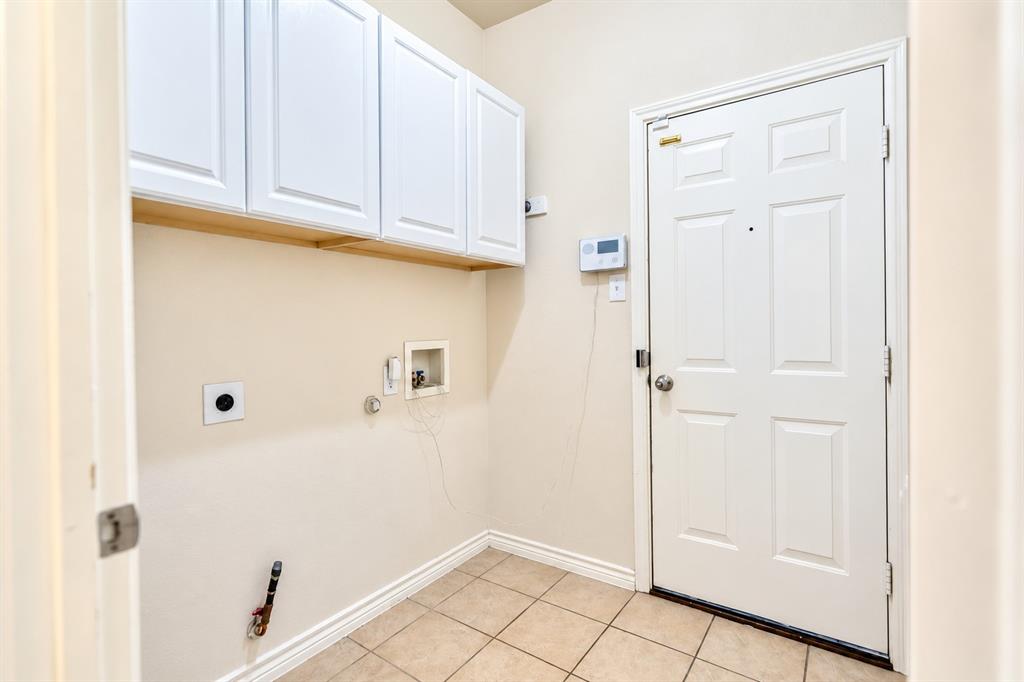 Wall-mounted white cabinetry, tile flooring, six-panel door, and laundry utility hookups