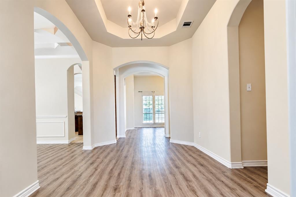 Foyer featuring wood-look LVP flooring, a tray ceiling, an integrated chandelier, and prominent arched architectural openings
