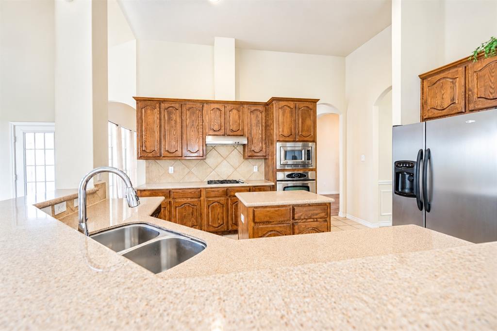 Kitchen featuring high-vaulted ceilings, granite countertops, stained wood cabinetry, stainless steel appliances, and a central island