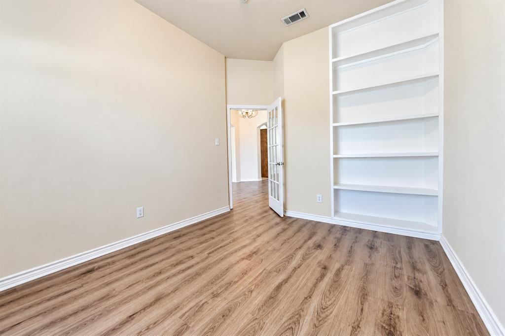 Room featuring wood-look LVP flooring, built-in white shelving, and a glass-paneled door