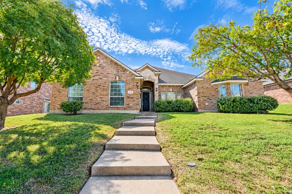 Brick exterior with multi-gabled roofline, arched entryway, concrete stairs, and mature landscaping Brick exterior with multi-gabled roofline, arched entryway, concrete stairs, and mature landscaping