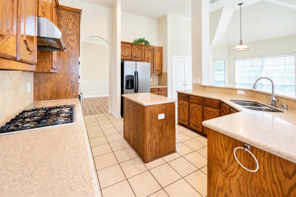 Kitchen featuring wood cabinetry, granite countertops, stainless steel gas cooktop, center island, and tile flooring