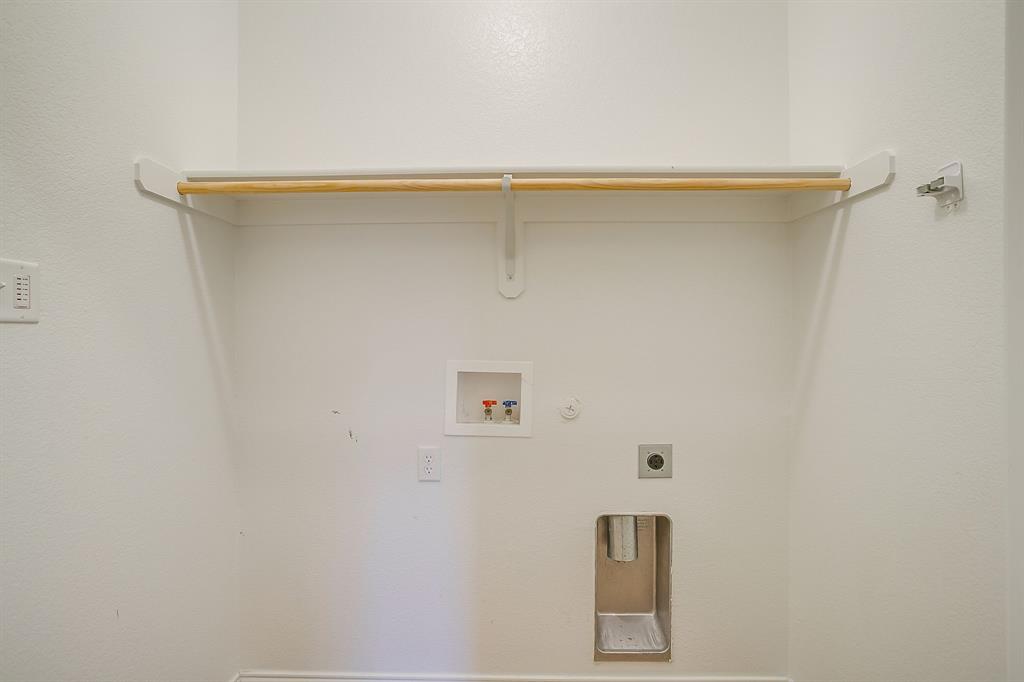 Utility alcove featuring a recessed plumbing connection box, metal dryer vent, and a mounted shelf with a wooden hanging rod