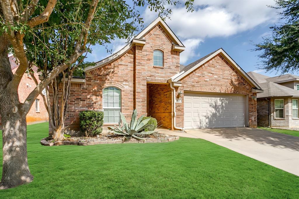 Brick exterior featuring a gabled roofline, arched window detail, concrete driveway, and established landscaping