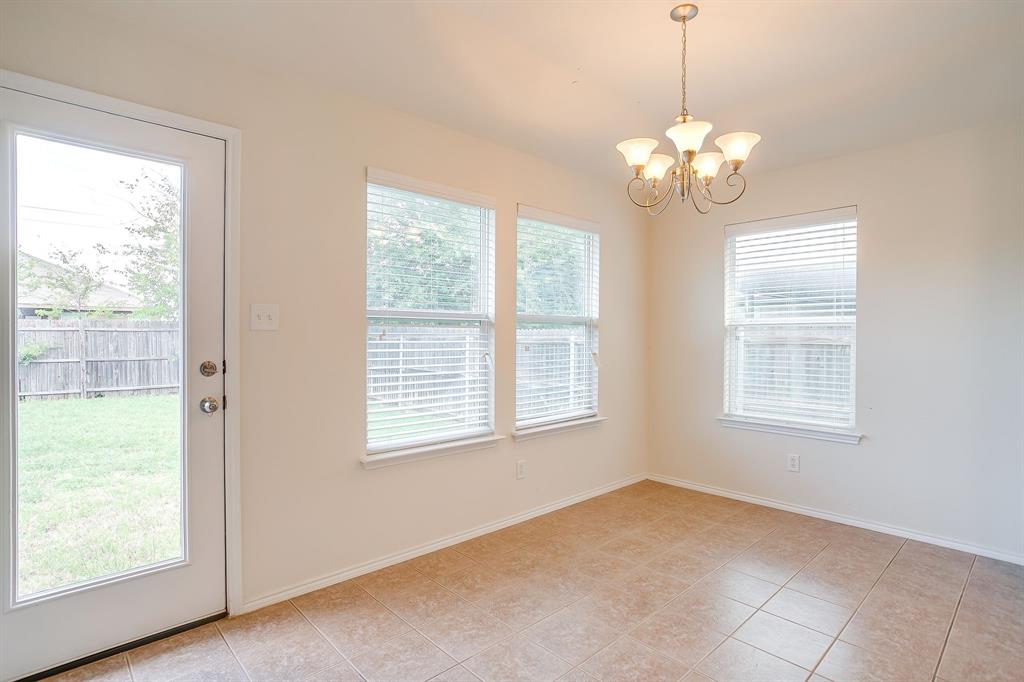 Neutral-toned tile flooring, three large windows with integrated blinds, and an exterior door with glass insert, complemented by a multi-arm metallic chandelier