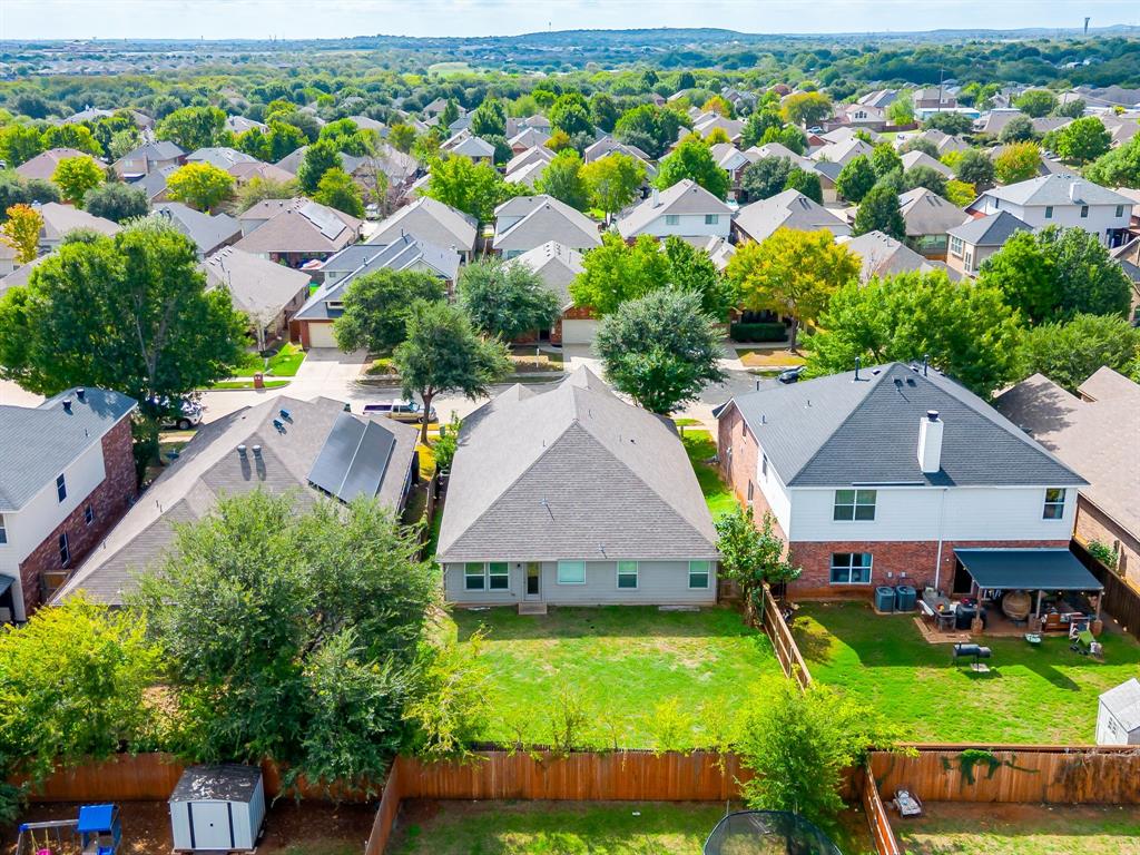 Aerial perspective featuring a multi-story residence with a composite shingle roof, brick and siding exterior, expansive rear lawn, and perimeter wood privacy fencing