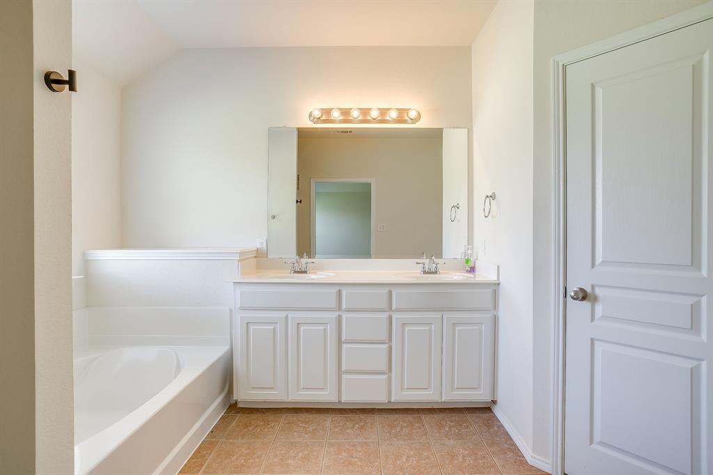 Bathroom featuring a dual-sink vanity with white cabinetry, a large wall-mounted mirror, an integrated soaking tub, and tile flooring