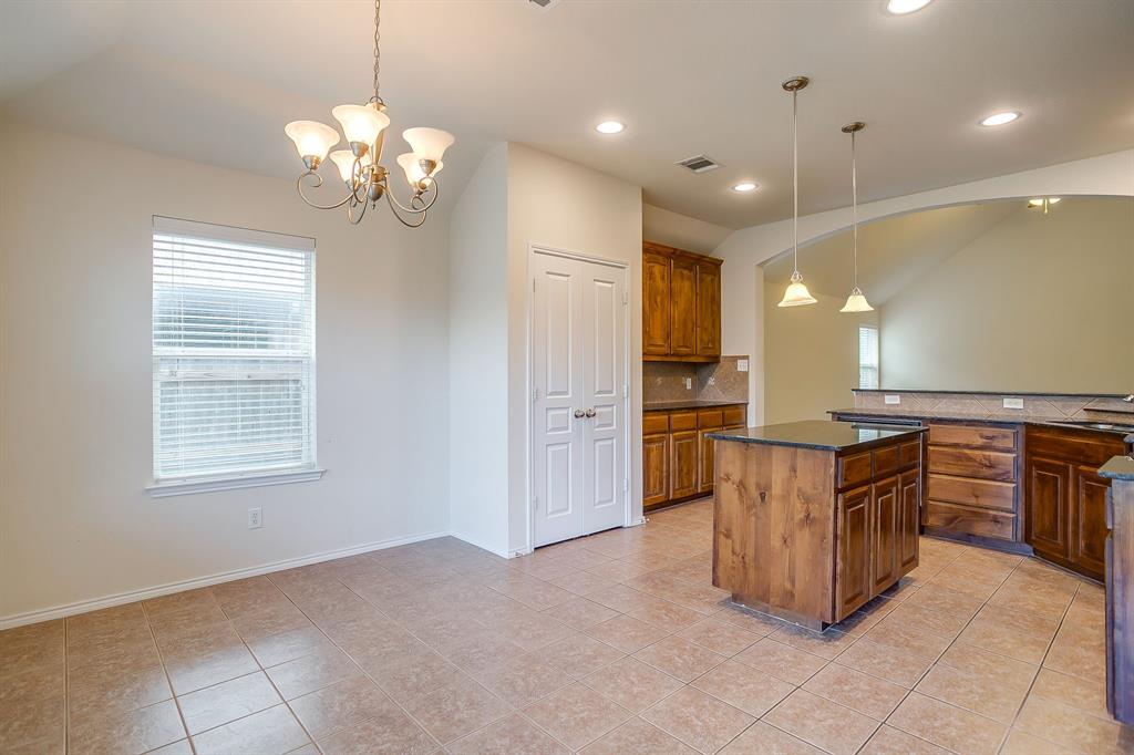 Kitchen featuring natural wood cabinetry, stone countertops, central island, dual hanging pendant lights, and decorative chandelier