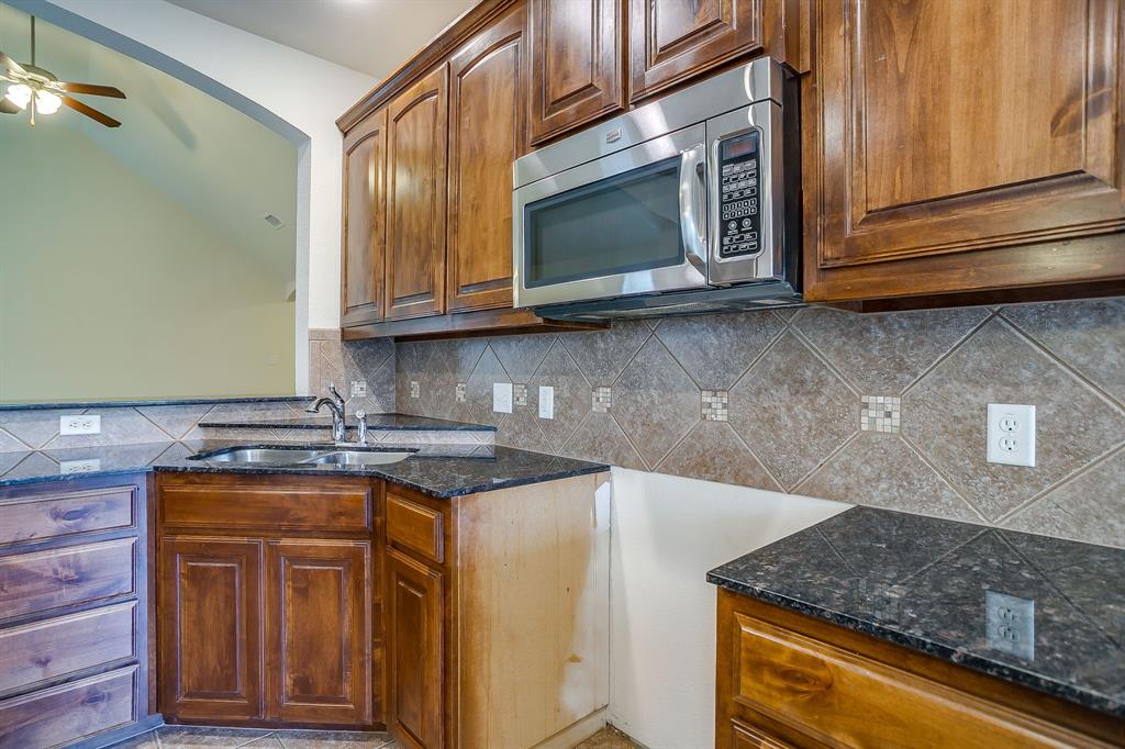 Kitchen featuring dark-toned cabinetry, stone-finish countertops, stainless steel over-the-range microwave, double-basin stainless steel sink with pull-out faucet, and a diagonal-set tile backsplash with decorative stone accents