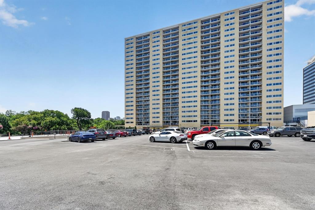 High-rise residential building featuring private balconies for each unit and an expansive, paved surface parking lot