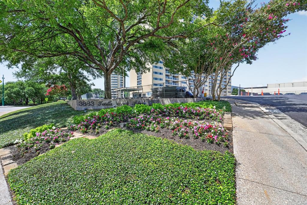 Landscaped exterior featuring mature canopy trees, tiered garden beds, seasonal flowering plants, and concrete retaining walls