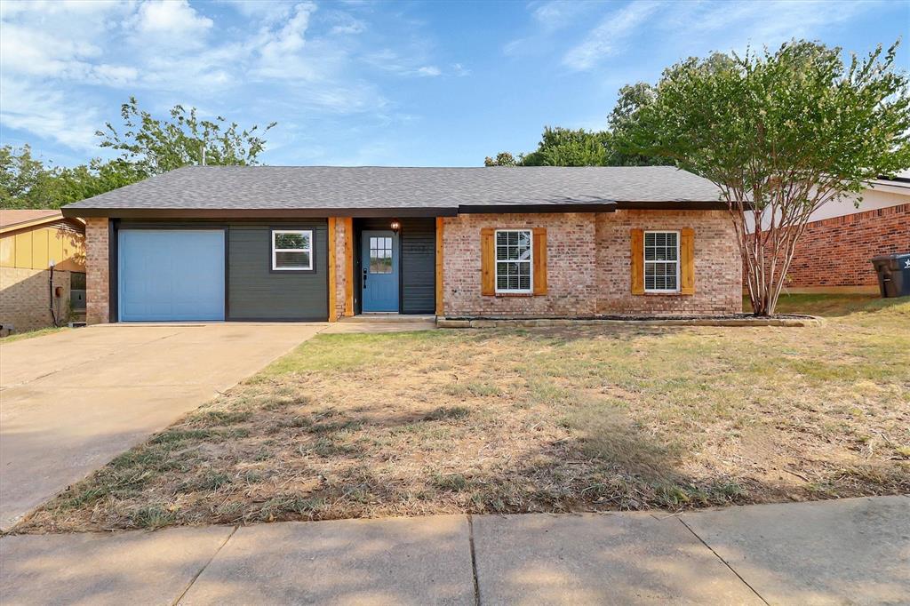 Single-story exterior featuring a brick facade, decorative wooden shutters, dark-toned siding accents, and a concrete driveway