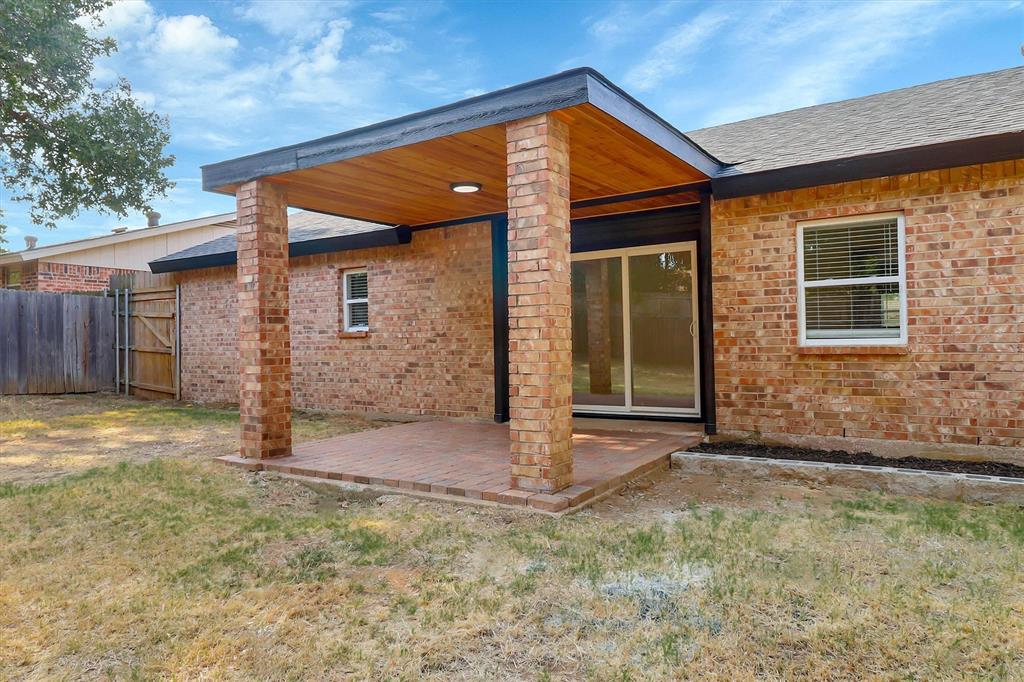 Covered brick patio featuring a wood-paneled ceiling, structural brick columns, and a sliding glass door entry