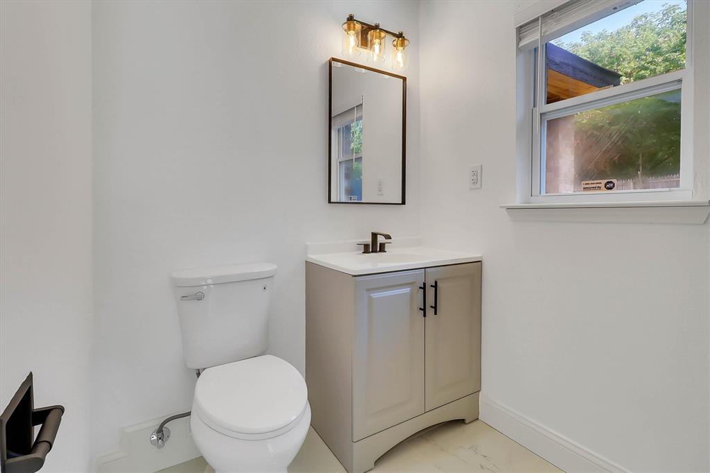 Vanity cabinet with a white countertop and rectangular sink, matte black hardware, wall-mounted mirror, three-light fixture, and ceramic flooring