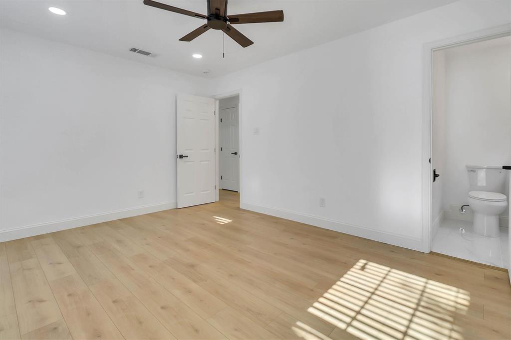 Room featuring light wood-finish flooring, recessed lighting, a dark-finish ceiling fan, and white doors with matte black hardware, accompanied by a separate restroom with white tile flooring and a porcelain commode