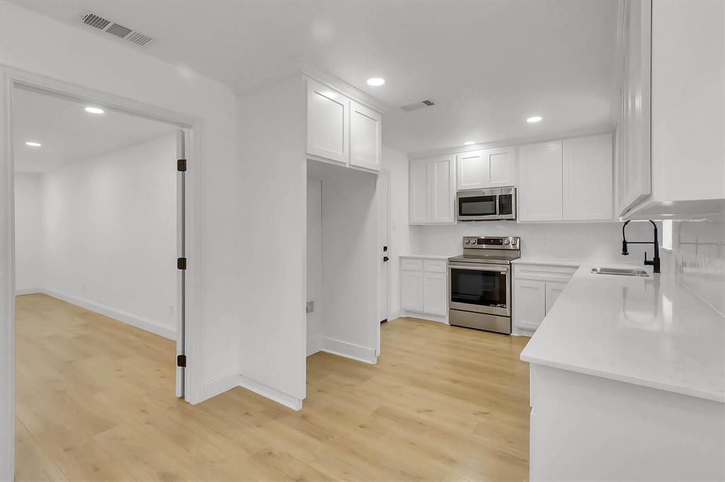 Kitchen featuring white shaker-style cabinetry, solid-surface countertops, stainless steel appliances, matte black plumbing fixtures, and wood-finish flooring