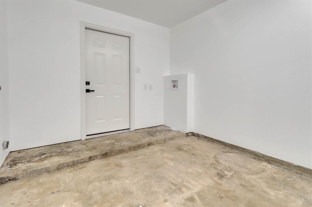 Utility area featuring a raised concrete platform, white-painted walls, an exterior-grade entry door with matte black hardware, and dedicated plumbing connections