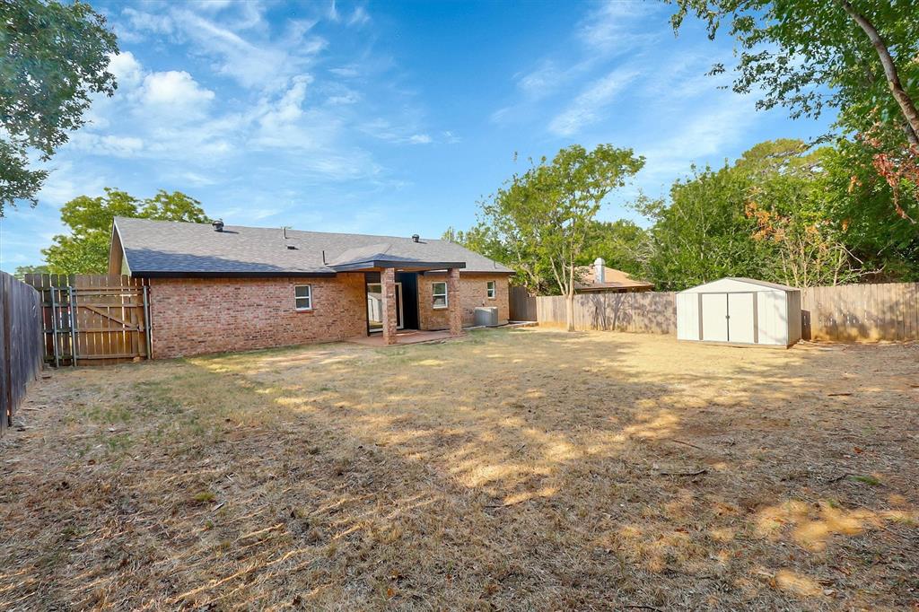 Brick exterior with a covered rear patio, wood-slat privacy fencing, and a detached storage shed