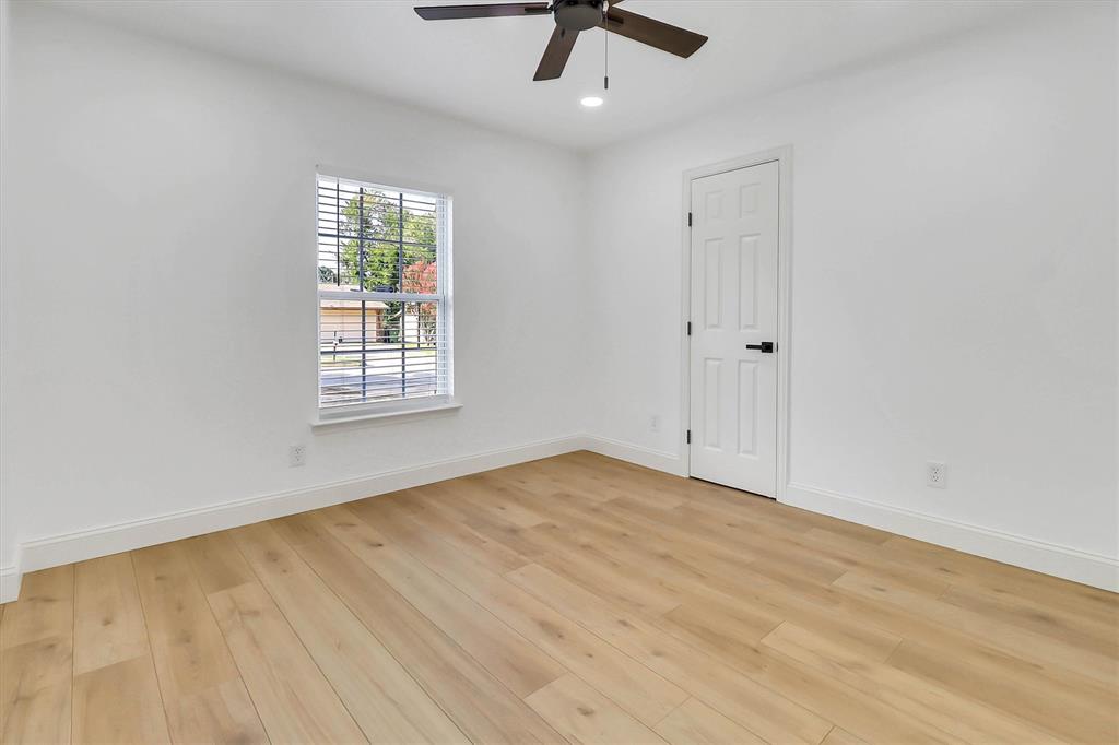 Light-filled room featuring wood-finish flooring, a ceiling fan, a single-panel interior door with matte black hardware, and a window with white casing