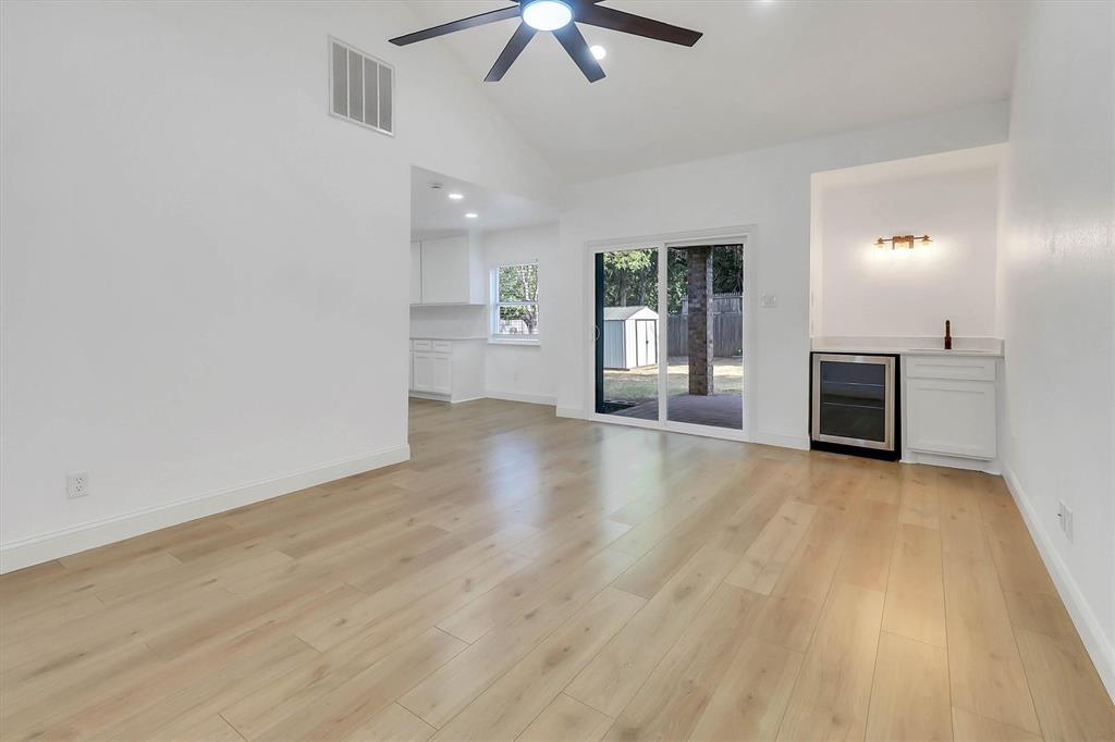 Vaulted ceiling with integrated ceiling fan, light-toned wood-finish flooring, and built-in wet bar featuring a glass-front beverage refrigerator