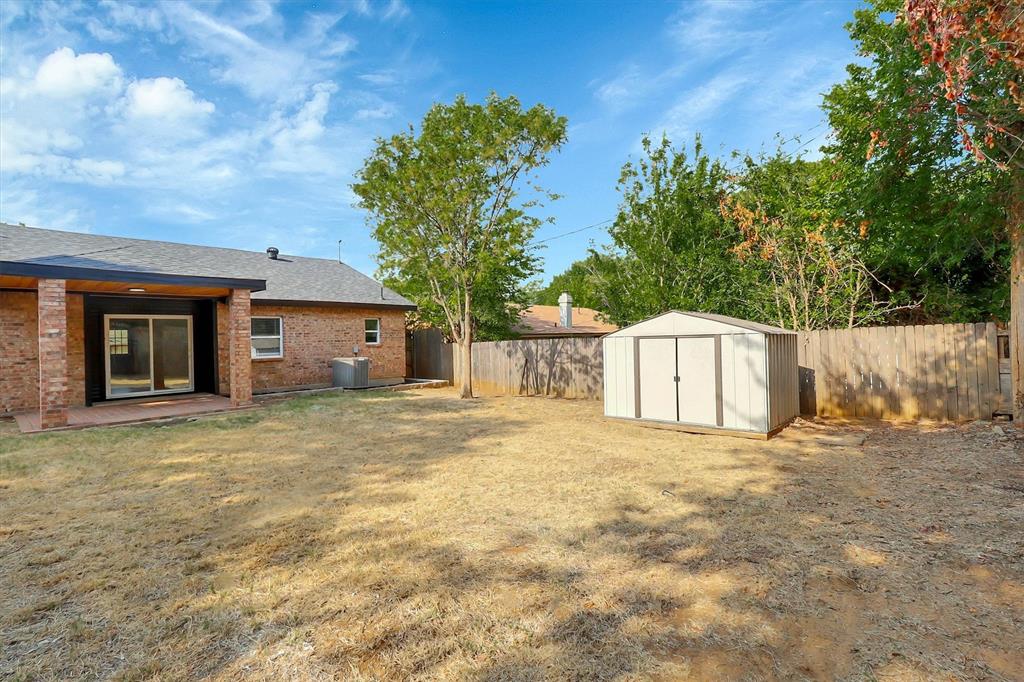 Rear brick exterior featuring a covered patio, detached storage shed, and perimeter wood fencing