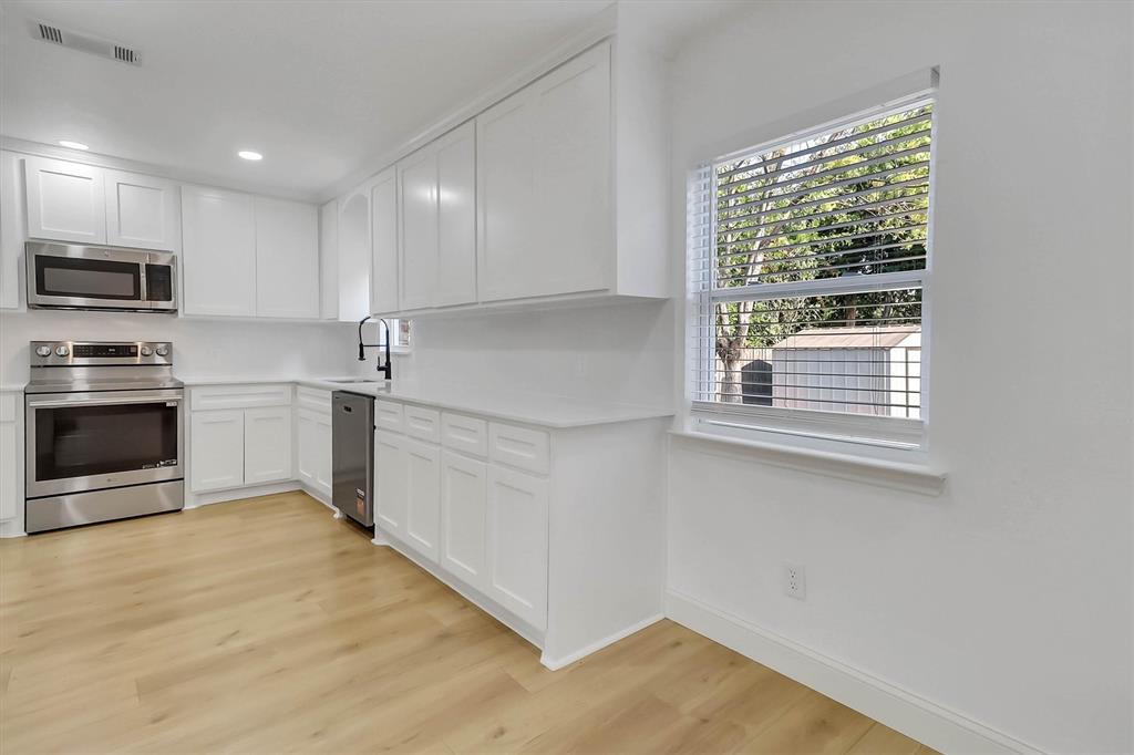 Kitchen featuring white shaker-style cabinetry, stainless steel appliances, light-toned wood-finish flooring, solid-surface countertops, and a gooseneck faucet