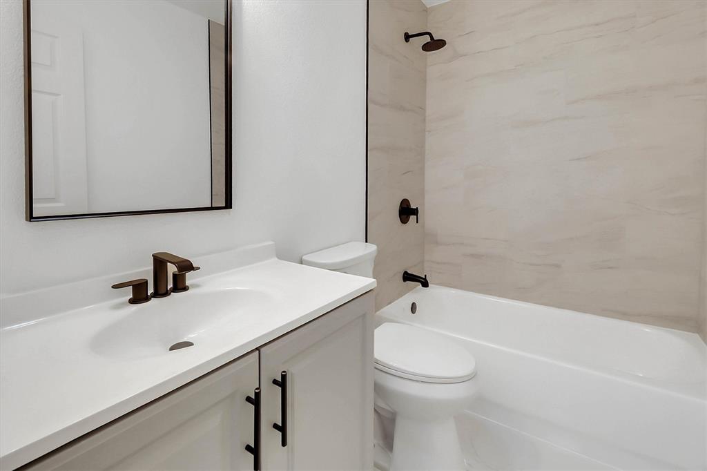 Bathroom featuring a white vanity cabinet with matte black hardware, a rectangular framed mirror, a porcelain tub surround with neutral-toned tile, and matte black plumbing fixtures