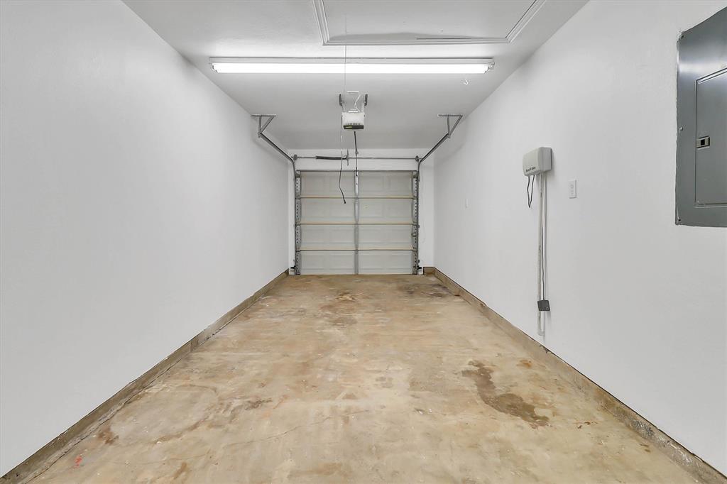 Single-car garage featuring a sectional overhead door, finished walls, fluorescent ceiling lighting, and an integrated electrical service panel
