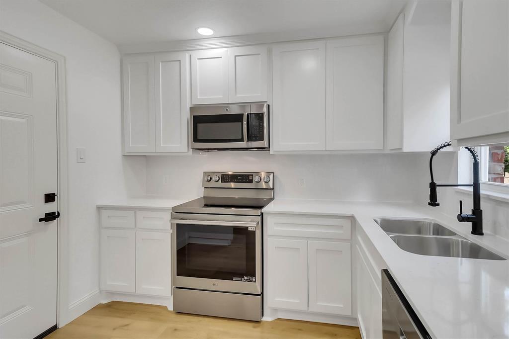 Kitchen featuring white shaker-style cabinetry, solid-surface countertops, stainless steel appliances, dual-basin sink with a matte black pull-down faucet, and wood-finish flooring