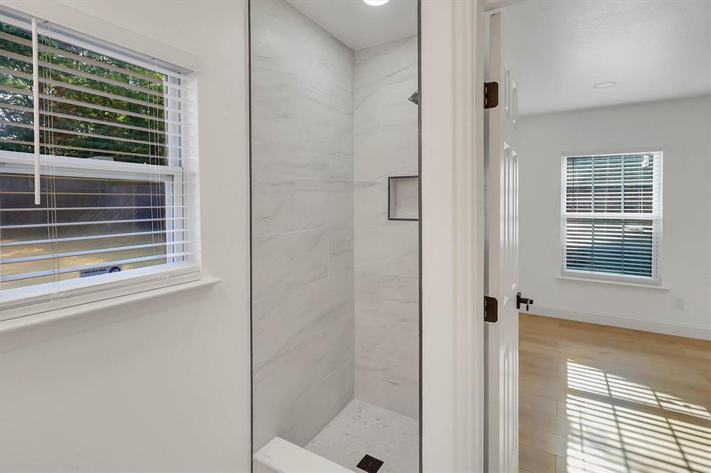 Walk-in shower featuring large-format stone-patterned tile, integrated recessed shelving, and a custom stone shower pan, complemented by wood-finish flooring and energy-efficient windows
