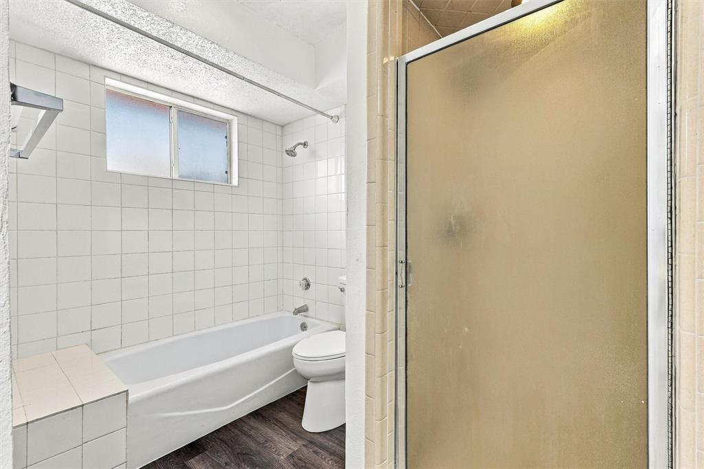 Bathroom featuring a built-in bathtub with a tile surround, separate shower enclosure with a glass door, wood-finish flooring, and a window