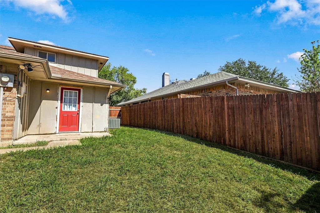 Rear exterior featuring a red entry door, horizontal wood-panel fencing, a concrete patio, and a grass lawn