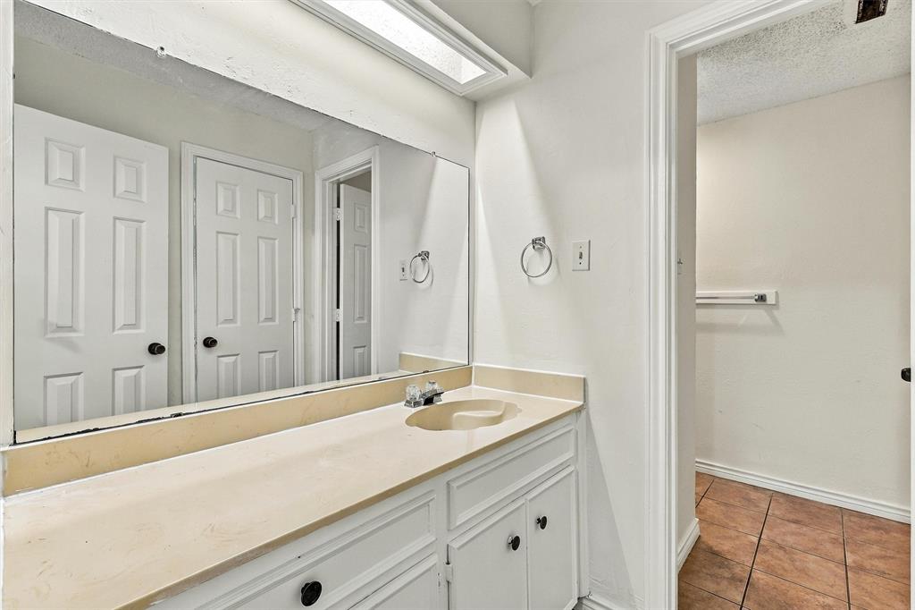 Built-in vanity with solid-surface countertop and integrated sink, full-width wall mirror, recessed overhead lighting, and tiled flooring