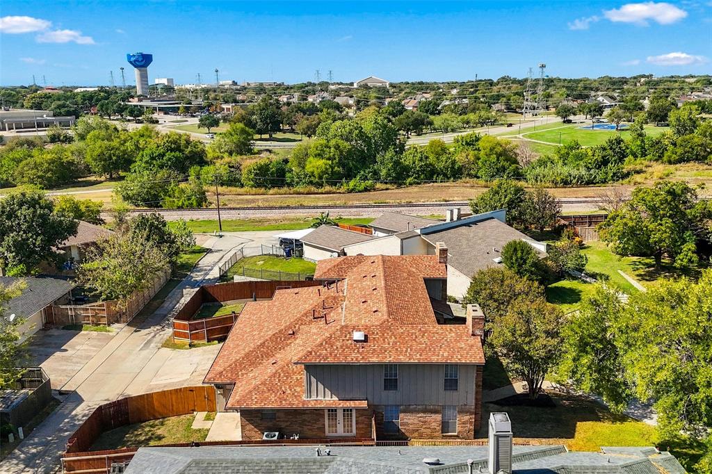 Aerial perspective of a multi-level structure featuring a multi-pitched composition shingle roof, brick and vertical siding exterior, wood-fenced perimeter, and dual masonry chimneys