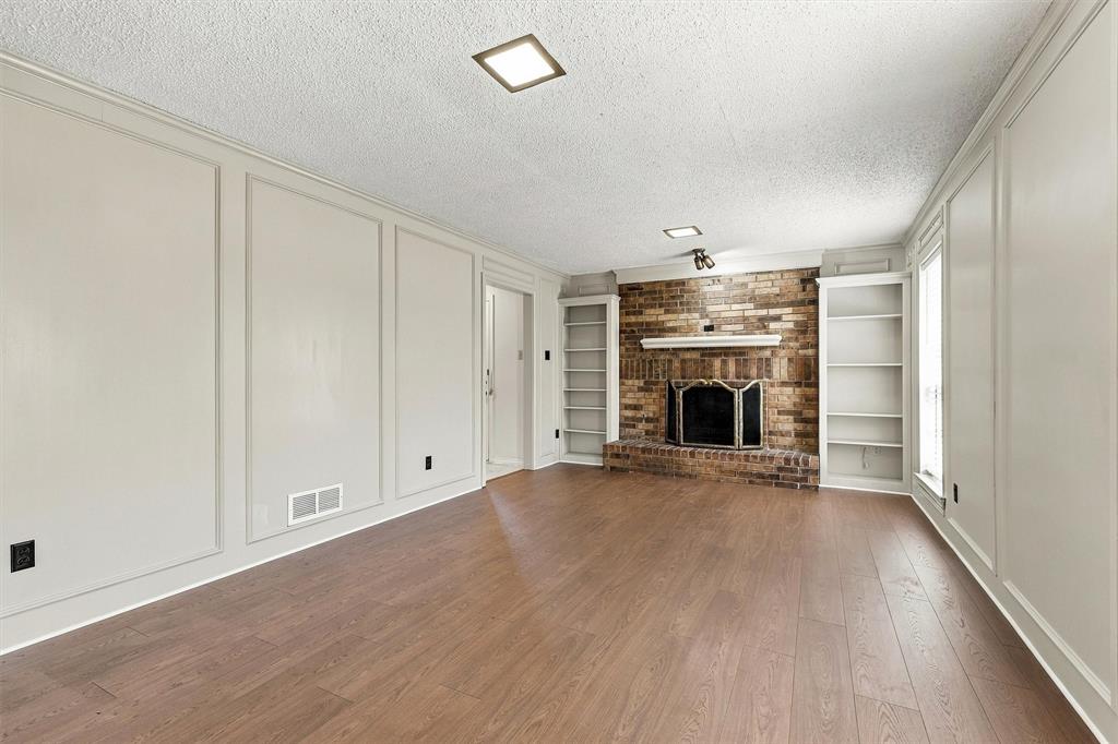 Living space featuring wood-finish flooring, floor-to-ceiling wainscoting, brick fireplace with a mantle, and built-in shelving