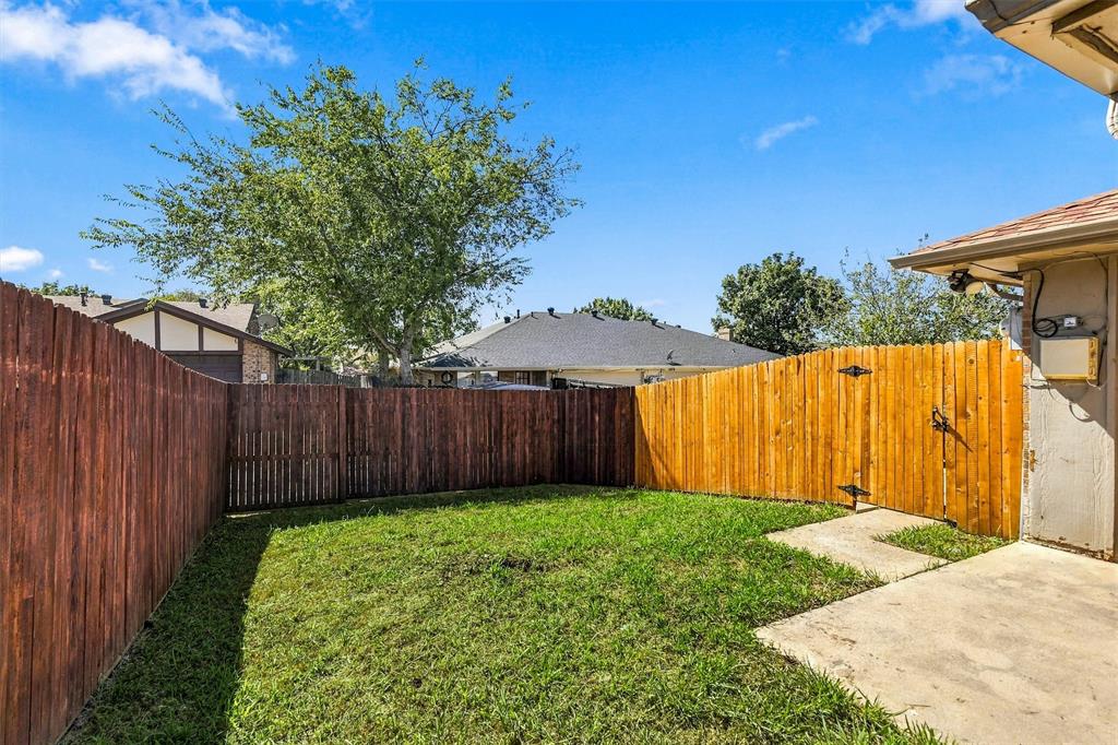 Fenced backyard featuring a grass lawn, concrete patio, and mature trees