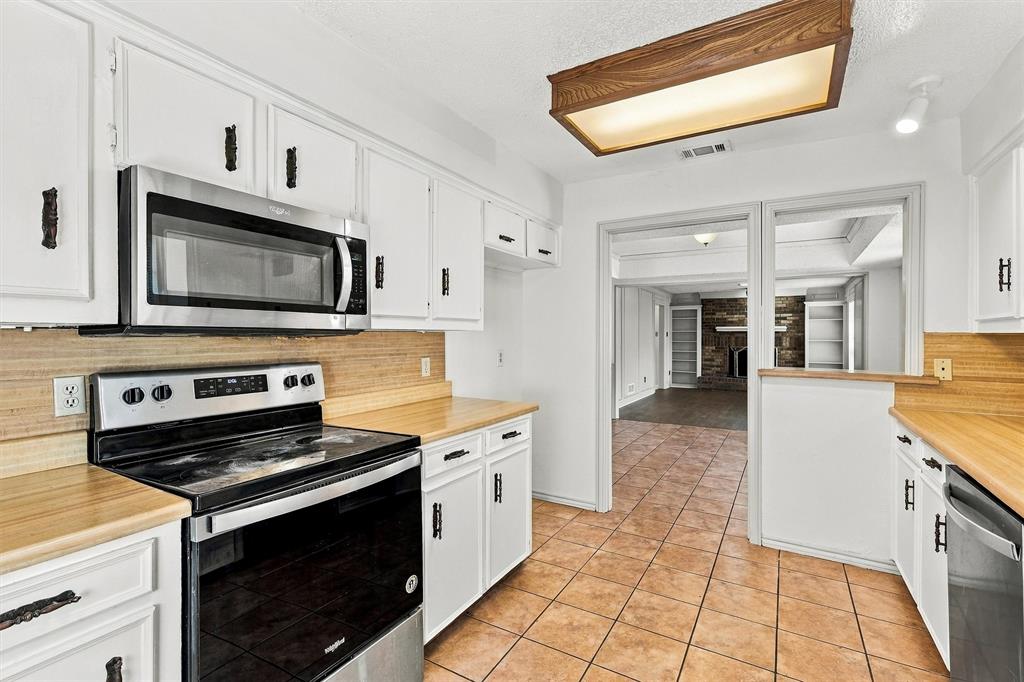 Kitchen featuring white cabinetry, wood-finish countertops, stainless steel appliances, tile flooring, and integrated overhead lighting