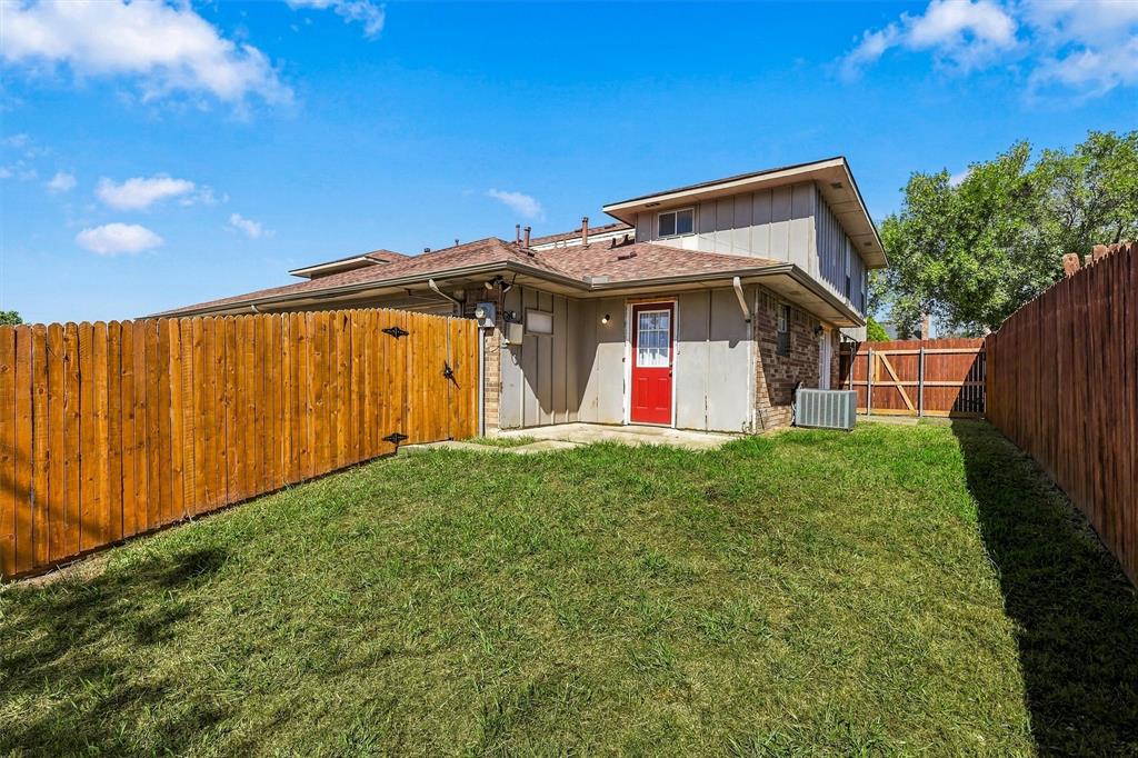 Rear exterior featuring a wood fence, concrete patio, grass lawn, and brick and vertical siding facade