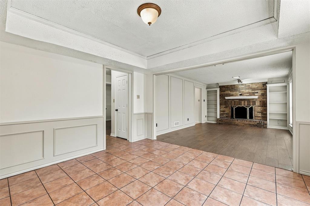 Interior featuring tray ceilings, wainscoting, tile flooring, wood-finish flooring, and a brick fireplace with built-in shelving