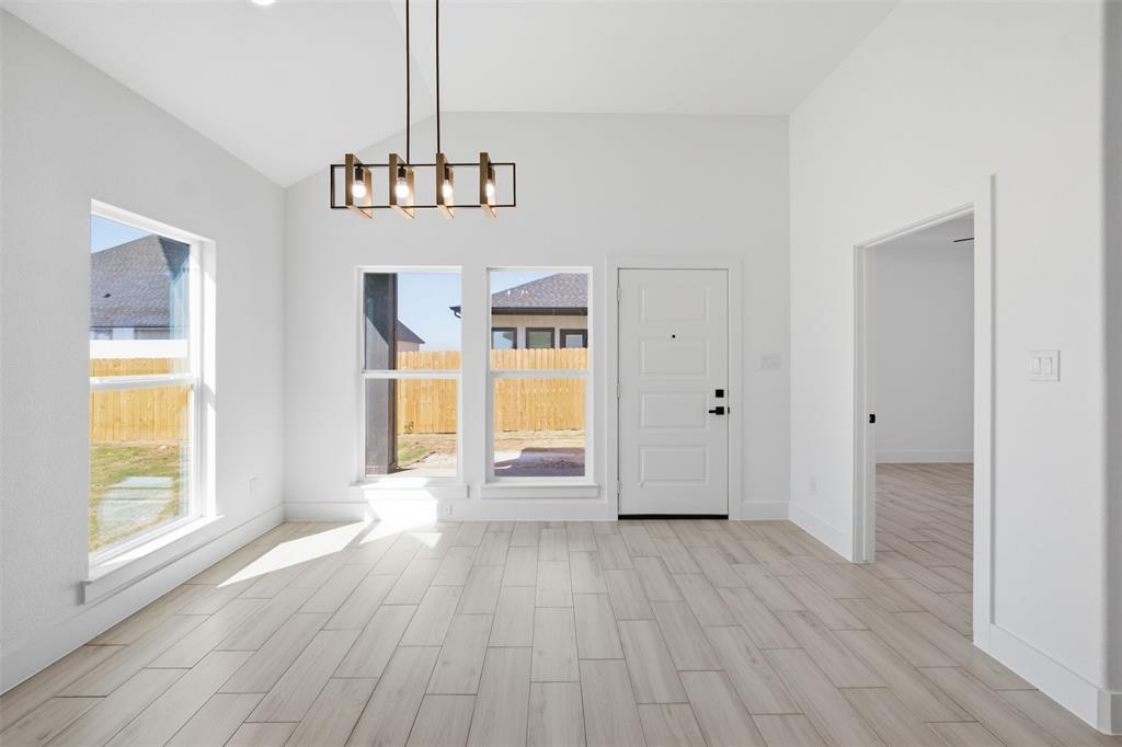 Vaulted ceilings, wood-finish tile flooring, geometric iron chandelier, and multiple windows with exterior exposure