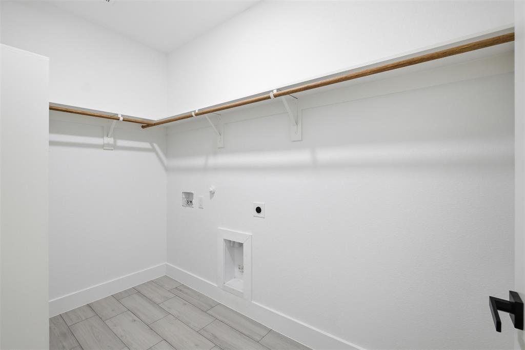 Walk-in storage space featuring wood-finish shelving rods, integrated laundry hookups, and wood-finish flooring