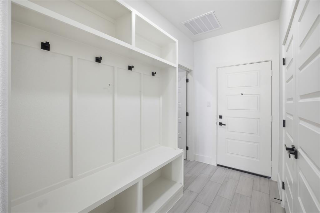 Built-in white storage cabinetry featuring upper shelving, integrated bench seating, and matte black hardware, accented by light-toned plank flooring and a four-panel door with matte black lever handles
